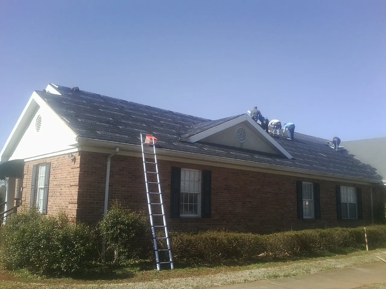 Crew tearing shingles off a brick ranch roof with a ladder set — Metal Roof Repair work by our crew in Lane City