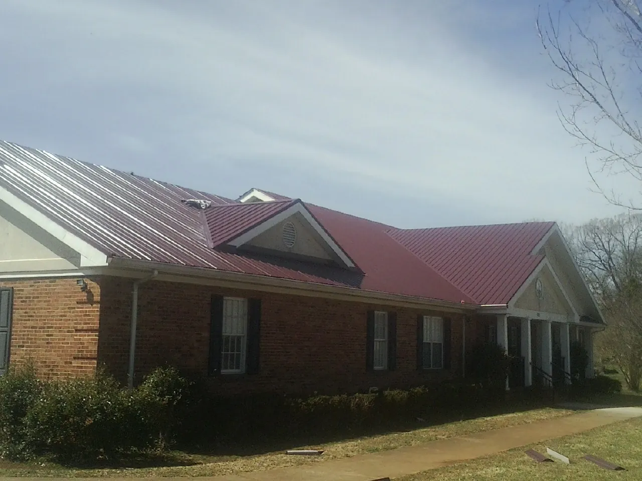 Red metal roof with gabled entries on a long brick building, from a Hail Damage Roof Repair job in Lane City