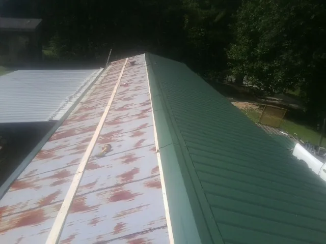 Old rusted panels beside newly installed green metal roofing — Wind Damage Roof Repair by Roofing Brothers in Lane City