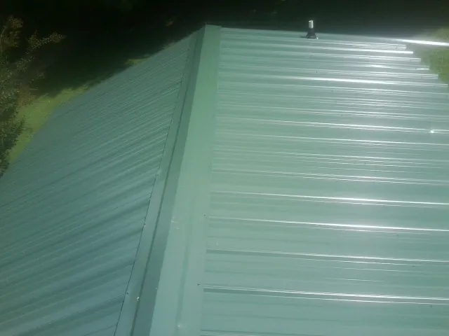 New green metal panels meeting at the ridge of a roof — Flat Roof Repair work by our crew in Lane City
