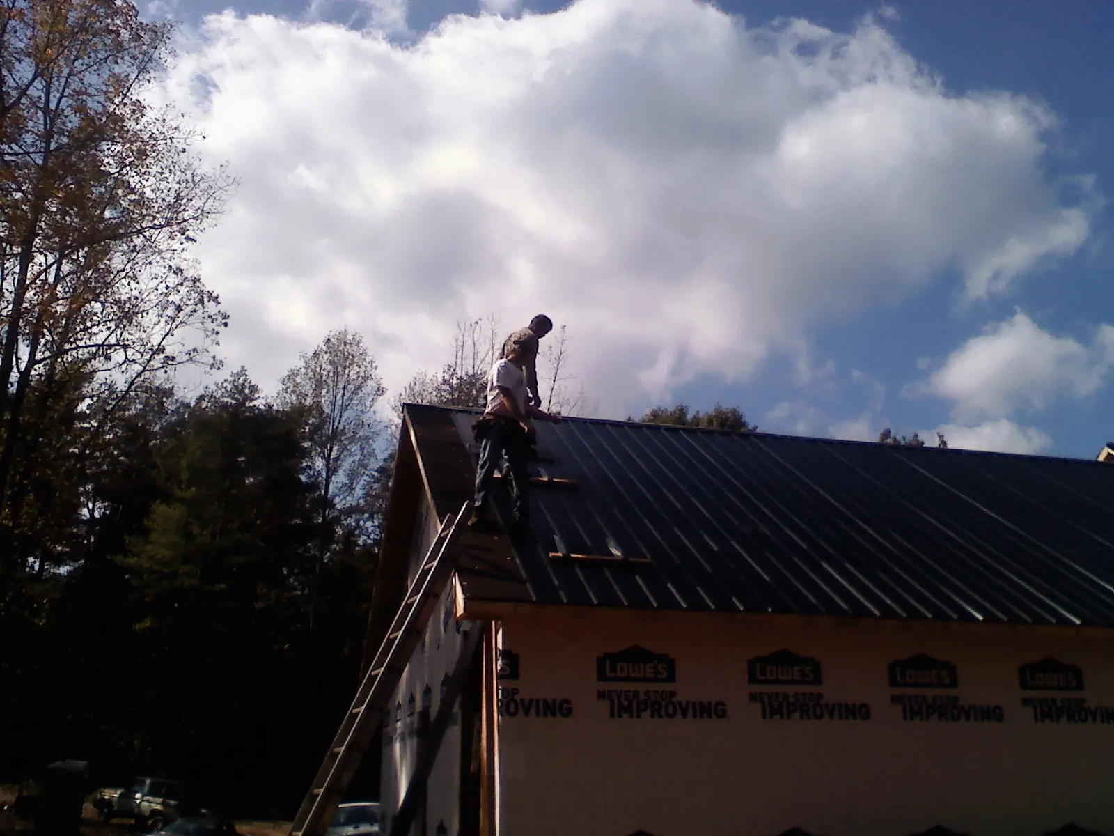 Roofer fastening dark metal panels high against a cloudy sky, from a Roof Inspection job in Lane City