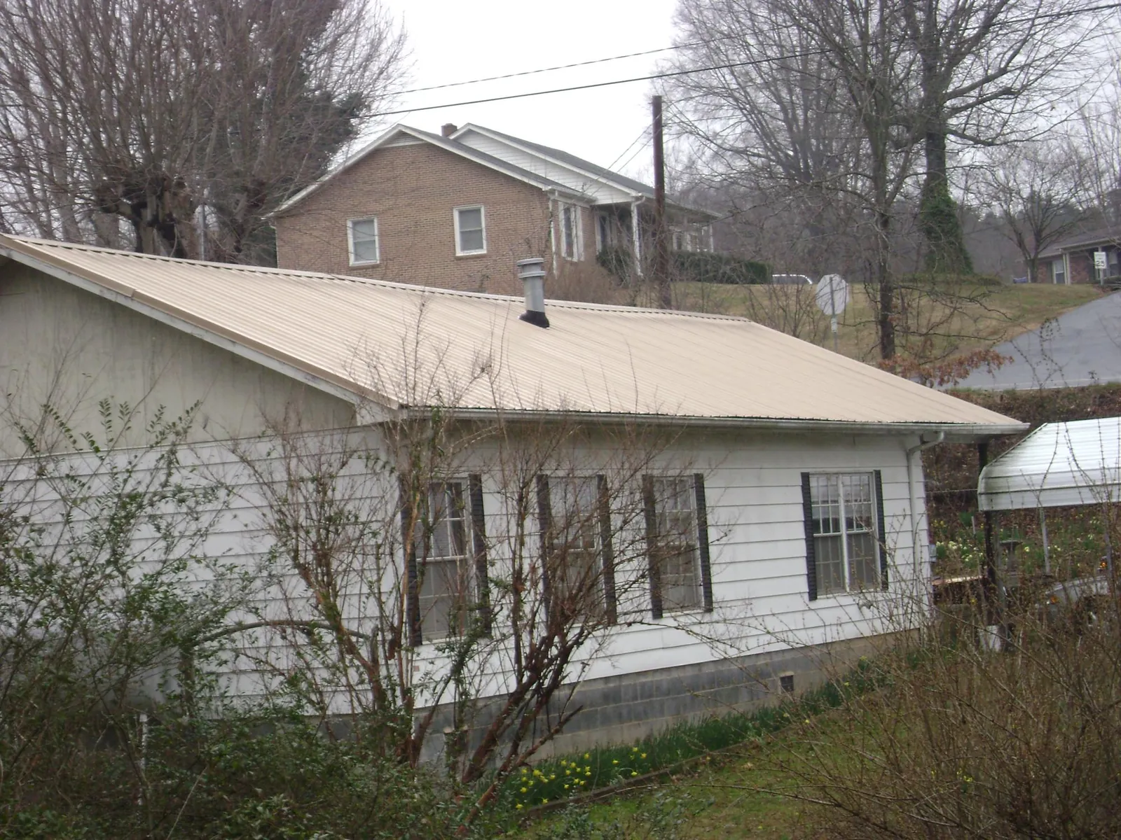 Tan metal roof on a white sided house set into a hillside — Commercial Roofing by Roofing Brothers in Lane City
